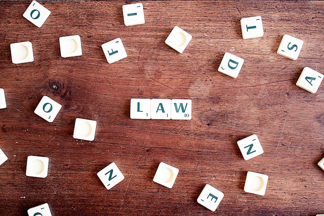 scrabble tiles that spell out “LAW” spread out on a wooden table